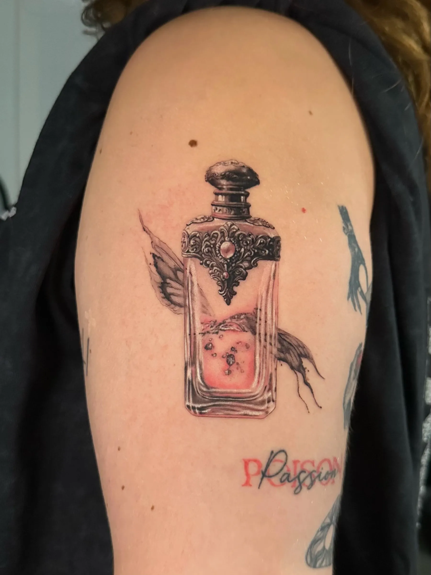 Frasco de perfume antiguo ornamentado con líquido rosado y alas de mariposa, en el brazo