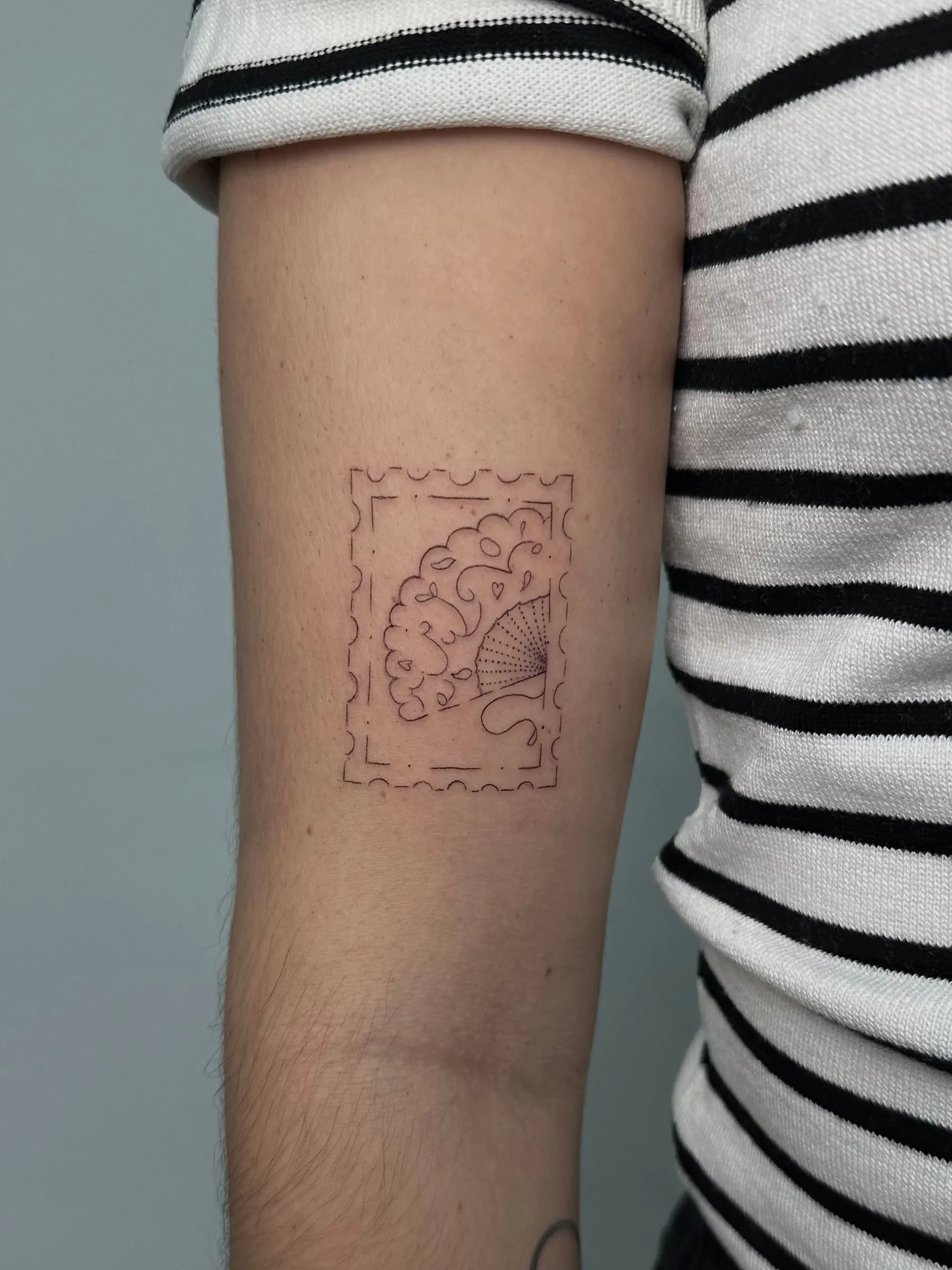 Sello postal en línea fina con un abanico abierto en su interior, en la parte trasera del brazo