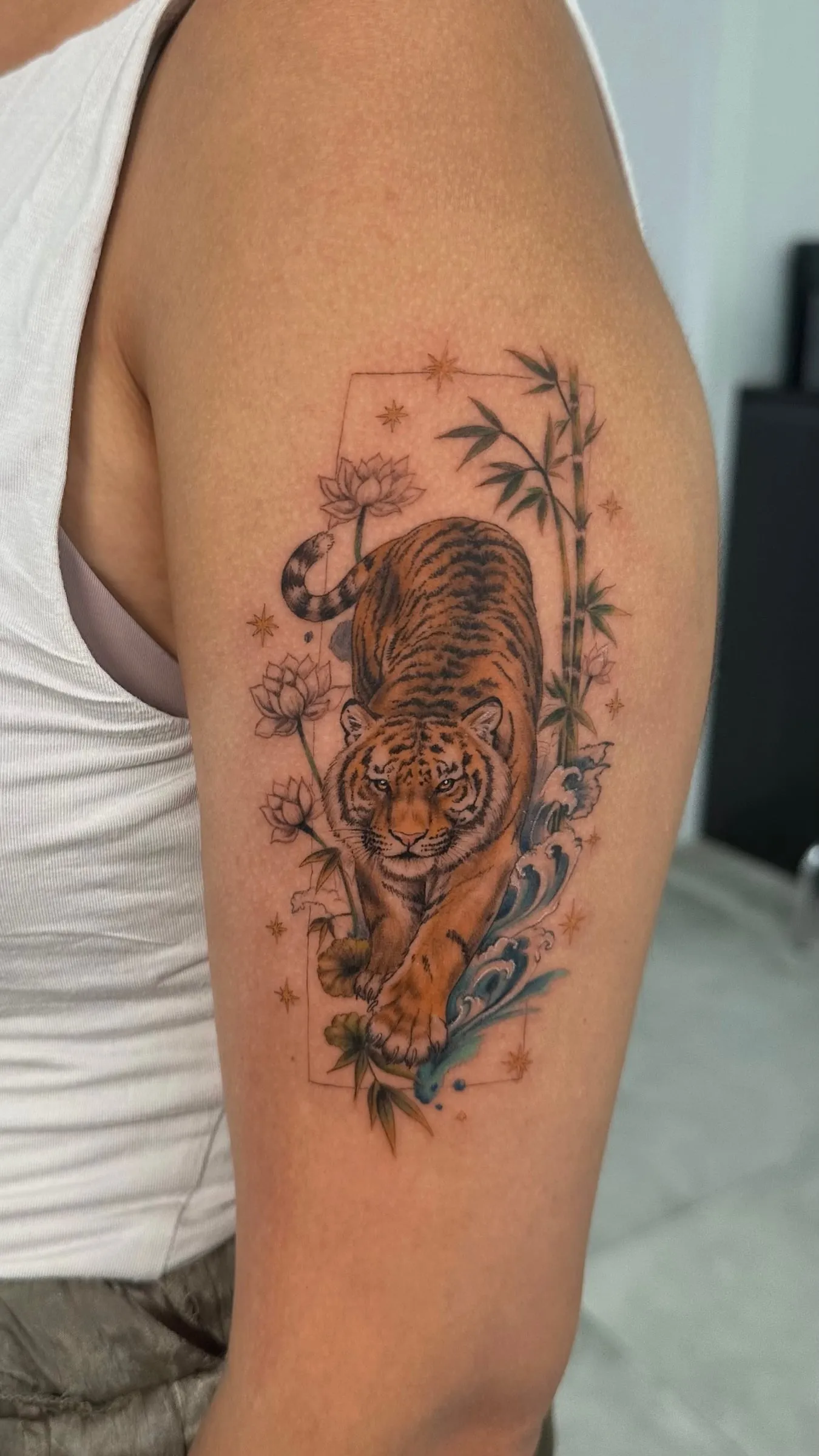 Tigre a color caminando entre flores de loto, bambú y olas, en el brazo