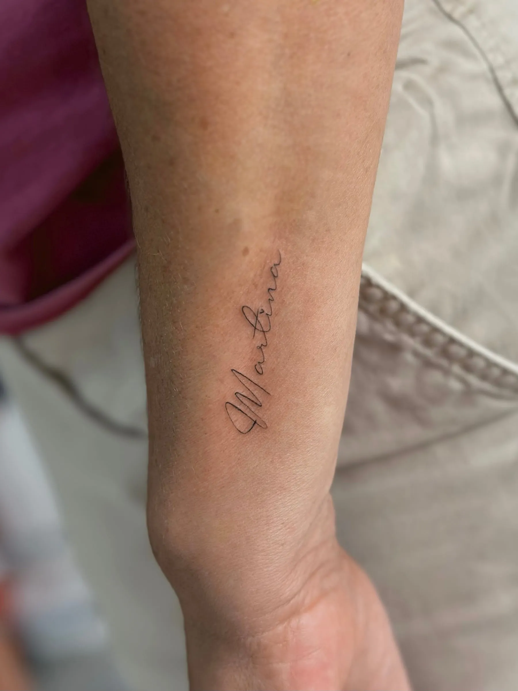 Nombre escrito en letra caligráfica de línea fina, en el antebrazo cerca de la muñeca