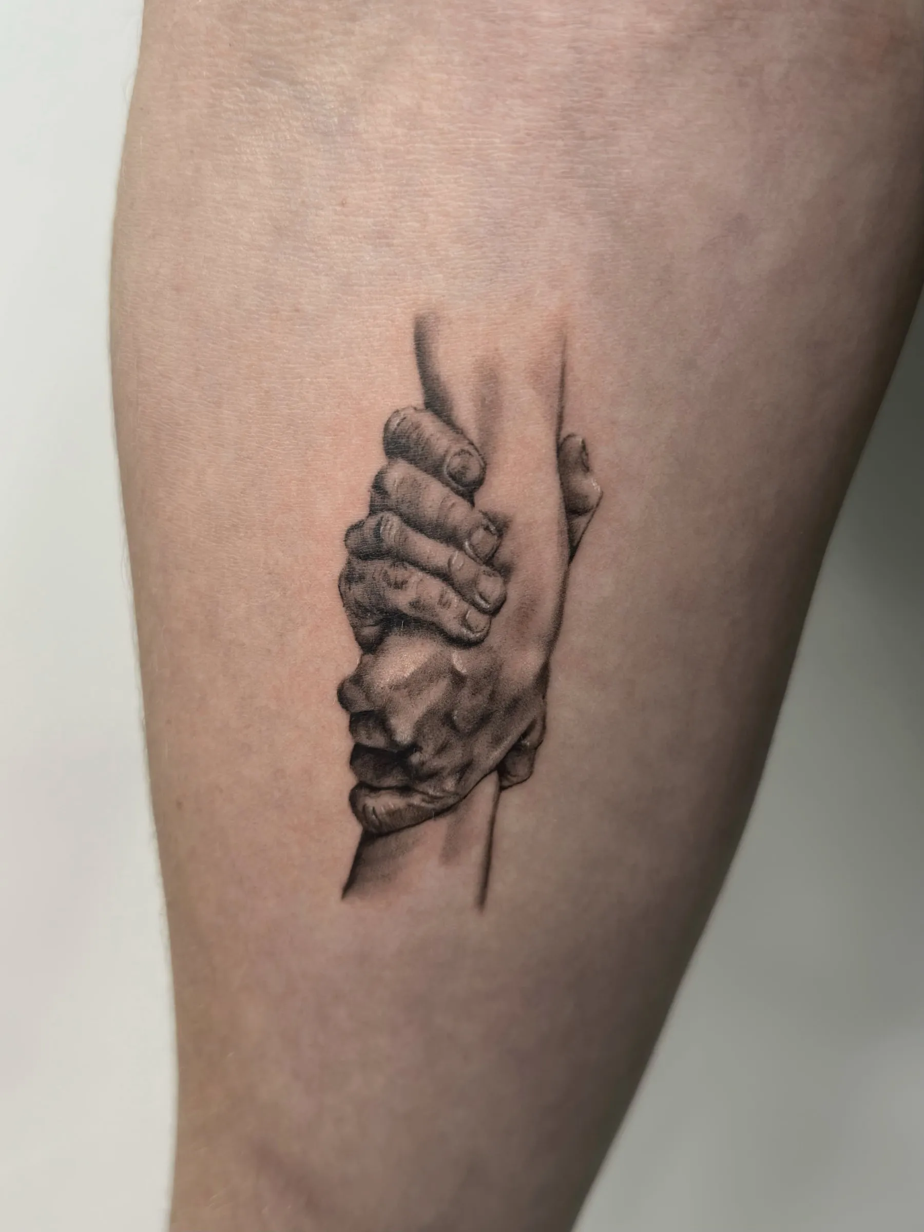 Dos manos realistas en negro y gris agarrándose con fuerza, en el antebrazo
