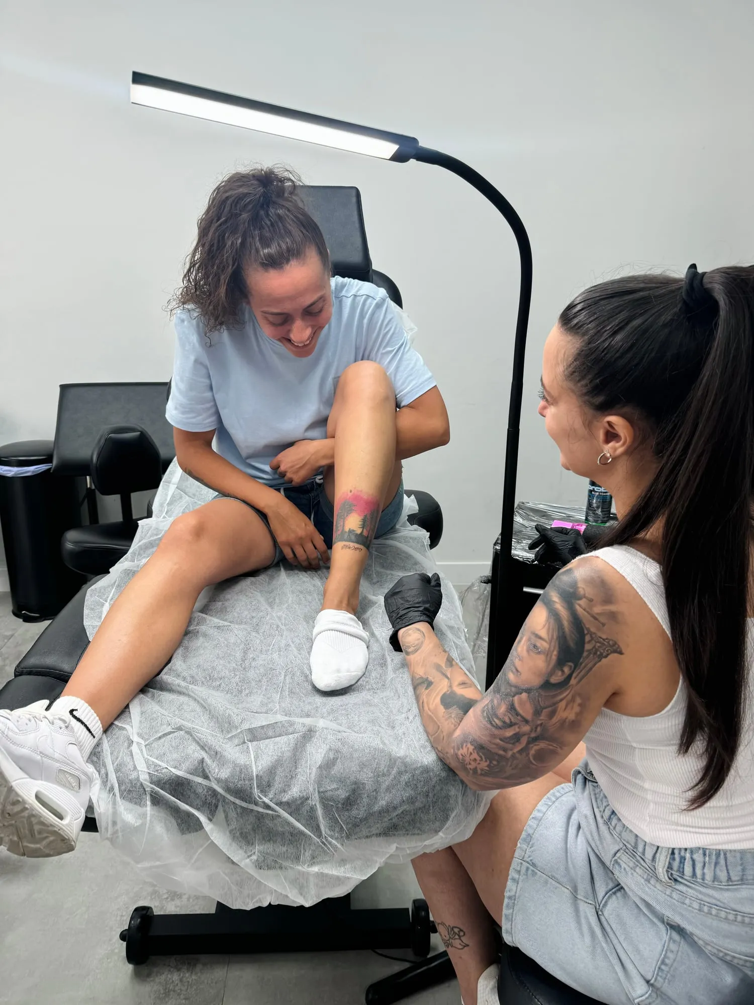 Tiffany durante una sesión con una clienta que se ríe mientras le enseña su pierna tatuada