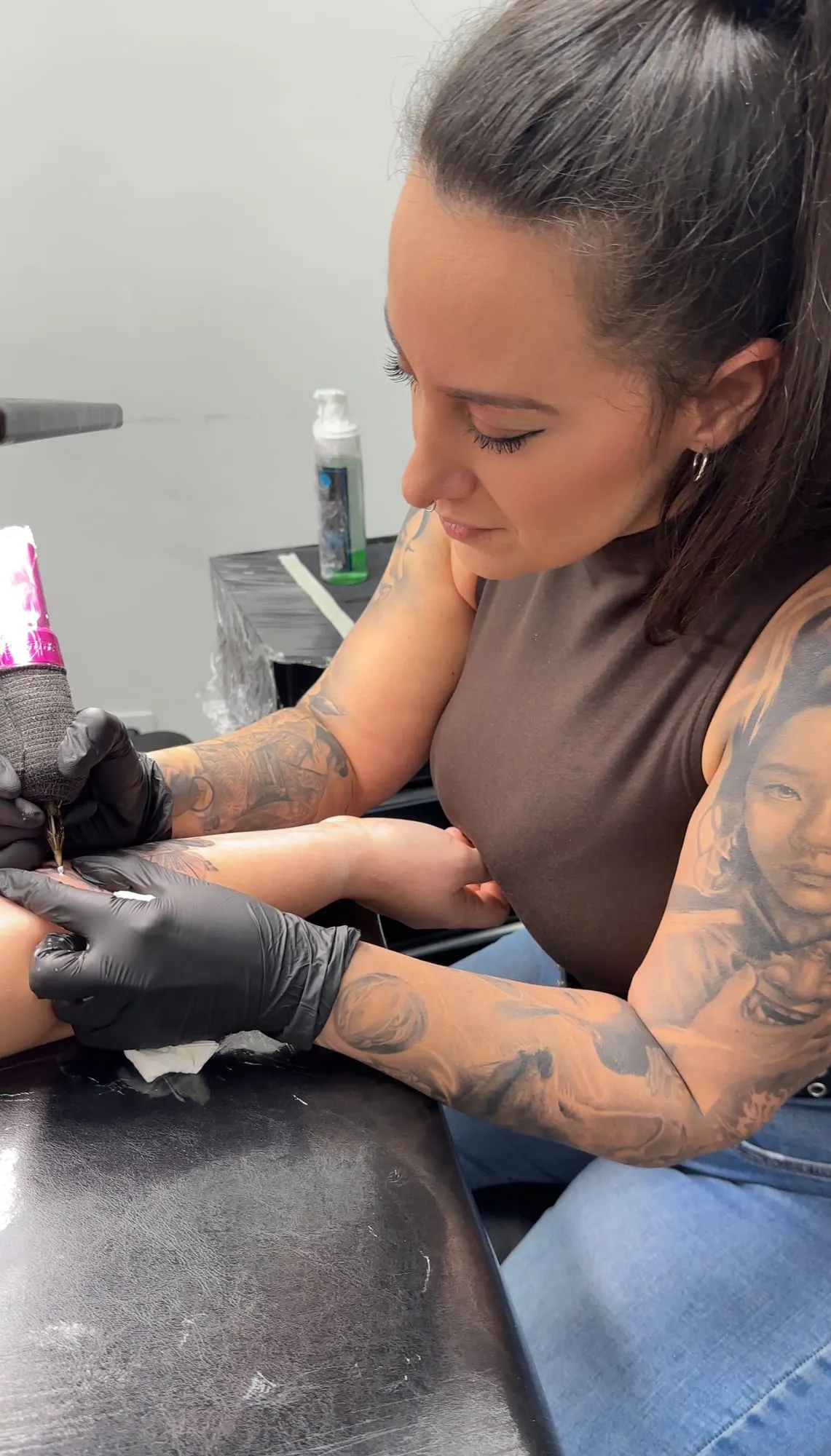Tiffany concentrada tatuando un brazo, con guantes negros